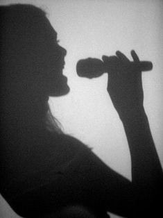 the silhouette of a woman holding a microphone in her right hand and looking into the distance