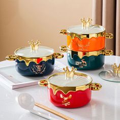 four different colored pots and spoons sitting on a table with gold trimming around them