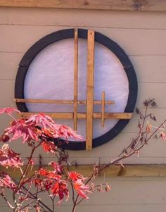 a round window on the side of a house with red leaves in front of it