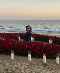 two people standing in front of flowers and candles on the beach with water behind them