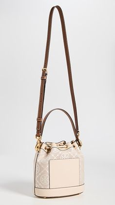 Find TORY BURCH T Monogram Bucket Bag on Editorialist. This Tory Burch bucket bag features a structured silhouette with gold-tone hardware. The bag is crafted from jacquard with a monogram pattern and leather trim. It has a drawstring top, patch interior pocket, and an optional adjustable strap. The bag is lined in suede and has a height of 8.25 inches, a length of 8.25 inches, and a depth of 4.75 inches. The strap drop is 21.75 inches and the handle drop is 4 inches. Monogram Canvas Pouch Shoulder Bag With Gold-tone Hardware, Gold Monogram Canvas Shoulder Bag With Double Handle, Monogram Canvas Bucket Bag With Detachable Handle, Gold Monogram Canvas Bag With Gold-tone Hardware, Designer Cream Bucket Bag, Gold Monogram Canvas Shoulder Bag With Dust Bag, Luxury White Bucket Shape Shoulder Bag, Luxury Cream Pouch Bucket Bag, Luxury Cream Bucket Bag In Pouch Shape