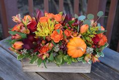 a wooden box filled with lots of flowers and pumpkins on top of a table