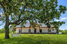 a white house sitting under a tree on top of a lush green field