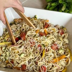 someone using chopsticks to stir noodles in a bowl with tomatoes, zucchini and cucumbers