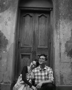 black and white photo of two people sitting in front of an old building with wooden doors