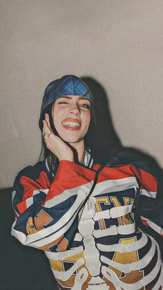 a woman with her hand on her face and wearing a baseball cap, standing in front of a wall