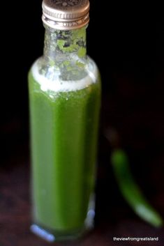 a bottle filled with green liquid sitting on top of a wooden table next to a pepper