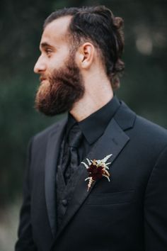 a man with a beard wearing a black suit and red flower boutonniere