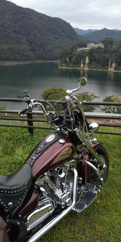 a motorcycle parked on top of a lush green field next to a lake with mountains in the background