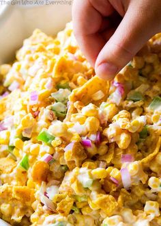 a person is dipping some kind of food into a white bowl filled with corn and onions