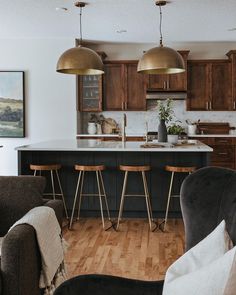 a kitchen with wooden flooring and bar stools next to an island in the middle