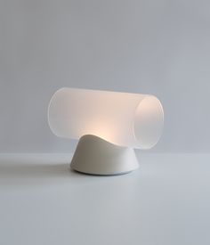 a white table lamp sitting on top of a gray floor next to a grey wall