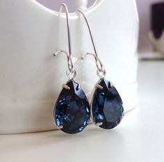 pair of earrings with blue crystal tears sitting on white surface next to coffee cup