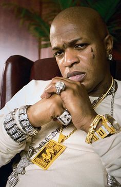 a man sitting in a chair with his hand on his chin and wearing jewelry around his neck