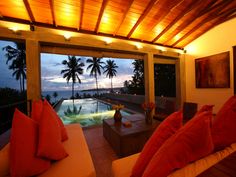 a living room filled with furniture and a large window overlooking the ocean at night time