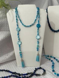 MOP Dyed 20mm flat (coin shape) beads with tiger eye blue/aqua chips and round faceted blue crystals create the lasso necklace. '' Tassels in aqua hang from each end of the 40-42 inch length of necklace...  Lasso style can be worn in so many ways - loop over or wrap twice and have ends hang independently.  Tassel ends are also adorned with layered square glass cube beads and round matte finish glass beads. This design is 1 of 4 designs created from the Blue Color Wave material selections featured in the video postings. #bluedesign  The video on this listing shows all 4 selection - you can find the other three listed under SKUs N-5002, N-5003, and N-5005. Bohemian Blue Round Beads, Adjustable Faceted Turquoise Beaded Necklaces, Blue Beaded Necklaces With Faceted Round Beads, Adjustable Blue Faceted Necklace, Blue Round Faceted Beaded Necklaces, Blue Faceted Beaded Necklace, Round Turquoise Faceted Beads, Lasso Necklace, 2024 Jewelry