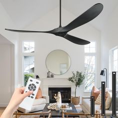 a person holding a remote control in front of a ceiling fan that is hanging from the ceiling