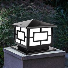 a light that is sitting on top of a cement block in front of some bushes