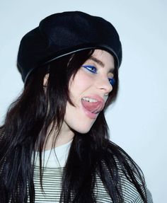 a woman with long hair wearing a black beret and blue eyeshadow smiling