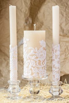 three candles with white lace on them sitting next to each other in front of hay