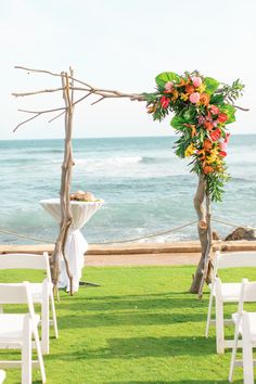 an outdoor ceremony set up with white chairs and flowers on the grass by the ocean