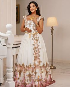 a woman standing in front of a piano wearing a white and pink dress with gold accents