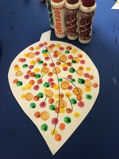 an art project made with crayons and glue on a blue tablecloth next to two cans of soda