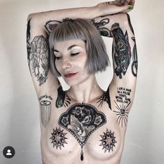 a woman with tattoos and piercings on her chest is posing for the camera while holding her hands behind her head