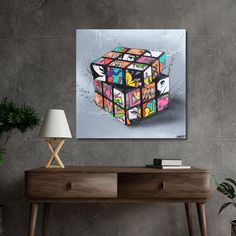 a table with a lamp and a painting on the wall above it that has a rubix cube