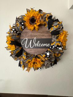 a welcome wreath with sunflowers and black ribbon hanging on the wall next to a door