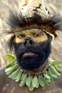 a man with black and gold paint on his face wearing a feather headdress