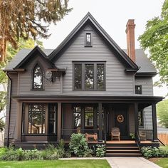 a large gray house with black trim and windows on the front porch, surrounded by greenery