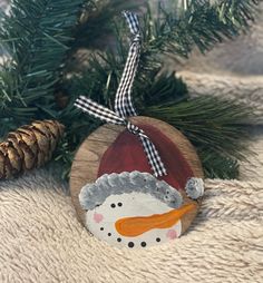 a wooden ornament with a snowman on it and pine cones in the background