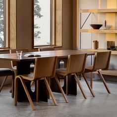 a dining room table and chairs in front of large windows with open shelves on either side