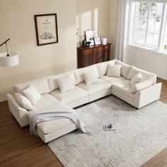 a white sectional couch sitting on top of a wooden floor next to a rug and window