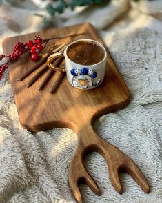 a cup of coffee sitting on top of a wooden cutting board with utensils