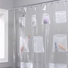 the shower curtain is clear and has various items hanging on it's hooks, along with other bathroom accessories