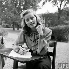 a black and white photo of a woman sitting at a table with a pen in her hand