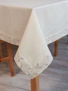 a white table cloth on top of a wooden chair with an embroidered design in the center