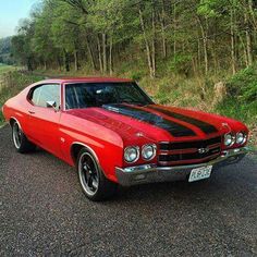 the red car is parked on the side of the road in front of some trees