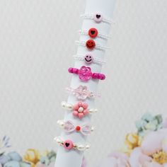 a stack of bracelets with hearts and buttons on them sitting in front of flowers