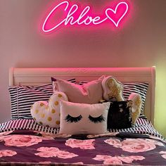 a pink neon sign above a bed with pillows