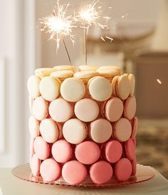 a cake decorated with pink, white and yellow cookies is topped with a sparkler