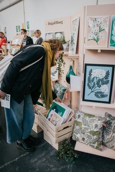 a woman looking at art on display in a room filled with people and other items