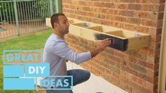 a man kneeling down next to a brick wall holding a piece of wood in front of him