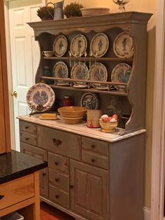 an old china cabinet with plates and bowls on it's top, in a kitchen