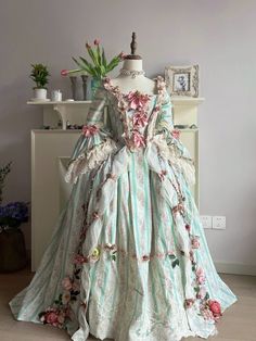 Indulge in the enchanting elegance of the Rococo and Baroque eras with our exquisite Marie Antoinette-inspired ball gown. This captivating dress, in a soft pastel green with charming pink floral accents, combines historical grandeur with modern sophistication, perfect for brides who desire a fairy-tale wedding. Rococo and Baroque Fusion: This gown masterfully blends Rococo and Baroque styles, featuring a structured bodice adorned with delightful pink bow ties and intricate floral embroidery. Lux Baroque Wedding Dress, Rococo Gown, Marie Antoinette Dress, Pastel Green And Pink, Wedding Dress With Bow, Marie Antoinette Dresses, Dress With Bow Tie, Baroque Wedding, Antoinette Dress