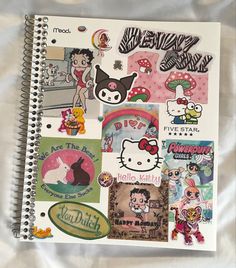 a spiral notebook with stickers on it and an image of hello kitty in the background