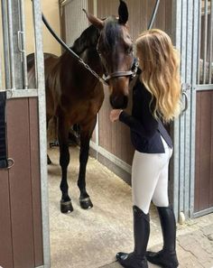 a woman standing next to a brown horse in a stall with another horse behind her