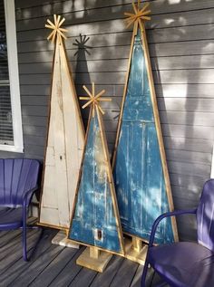 two wooden christmas trees sitting on top of a porch next to purple chairs and a blue chair